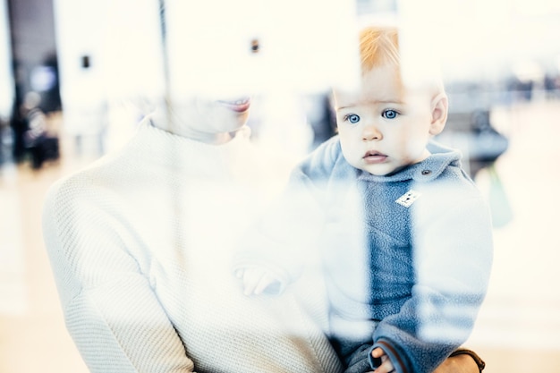 Zorgvuldige jonge moeder kijkt door het raam met zijn baby baby jongen kind terwijl hij wacht op