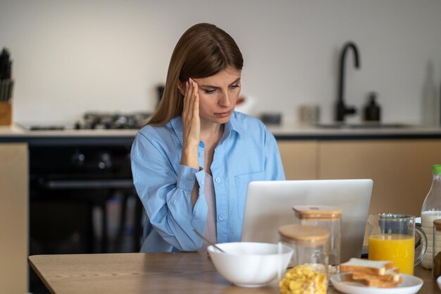 Foto zorgwekkende vrouwelijke huisvrouw kijkt naar laptop scherm aanraken hoofd