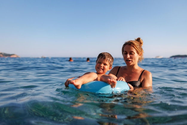 Zorgzame moeder berijdt haar zoon op een opblaasbare ring in de zee