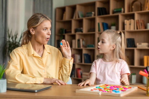 Zorgzame moeder die kleine kleuterdochter leert die woorden en letters correct uitspreekt