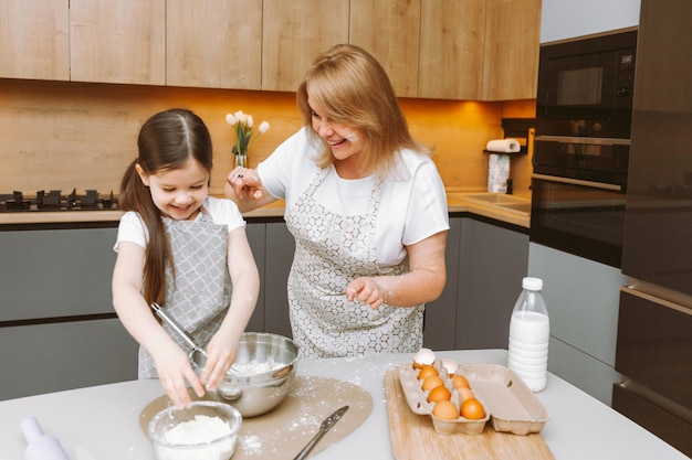 Zorgzame oma en kleindochter hebben plezier samen koekjes bakken in de thuiskeuken Een liefhebbende bejaarde oma en kleindochter bereiden een heerlijke zoete cake