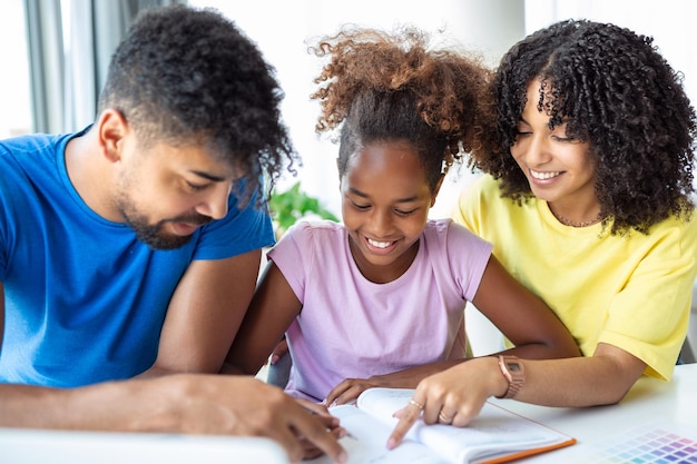 Zorgzame ouders helpen dochtertje met huiswerk thuis liefdevolle vader en moeder met een klein afro-amerikaans meisje dat samen in de keuken studeert op quarantaine homeschooling concept