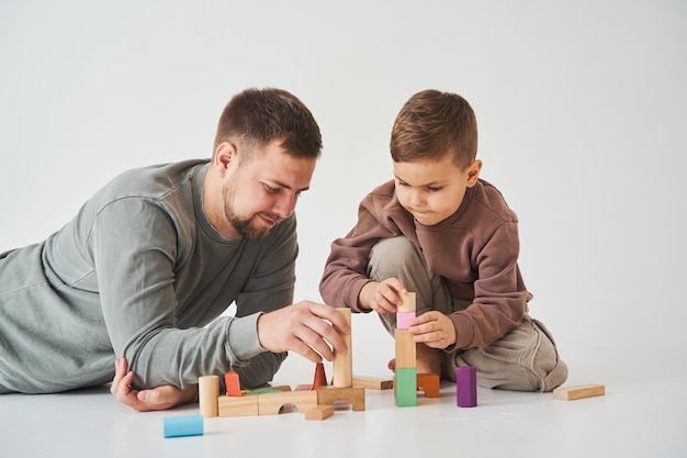 Zorgzame vader speelt met vrolijke zoon met houten speelgoedblokjes op witte achtergrond Vaderschap en kinderopvang