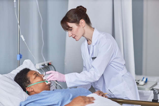 Zorgzame verpleegster die zuurstofondersteuningsmasker plaatst op oudere patiënt in ziekenhuiskamer