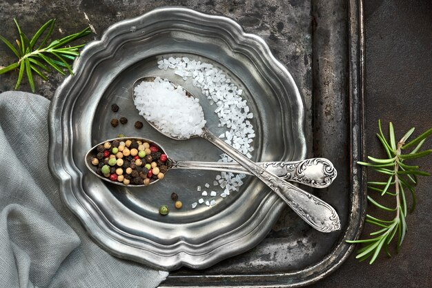 Zout in gemengde peper in vintage lepels op oude metalen plaat met linnen servet op donkergrijs