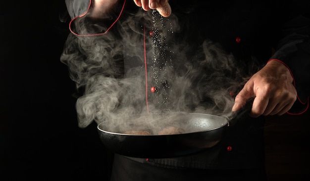 Zout toevoegen aan vleessteaks in een hete pan met stoom in de handen van een professionele kok