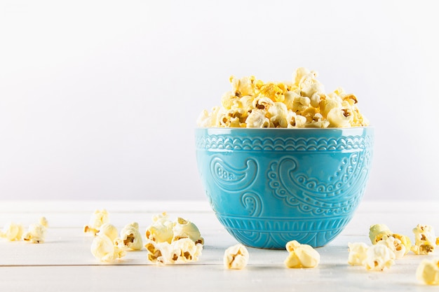 Zoute popcorn in een blauwe kop is op een houten tafel. Popcorn ligt rond de kom.