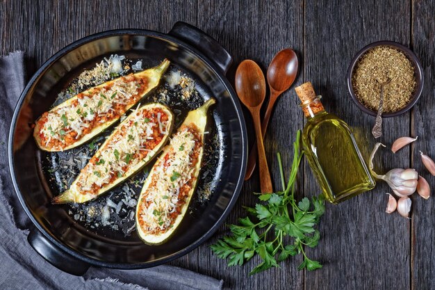 Zucchini boats stuffed with ground meat, chopped tomatoes, and cheese in a black baking dish on a wooden table,  italian cuisine