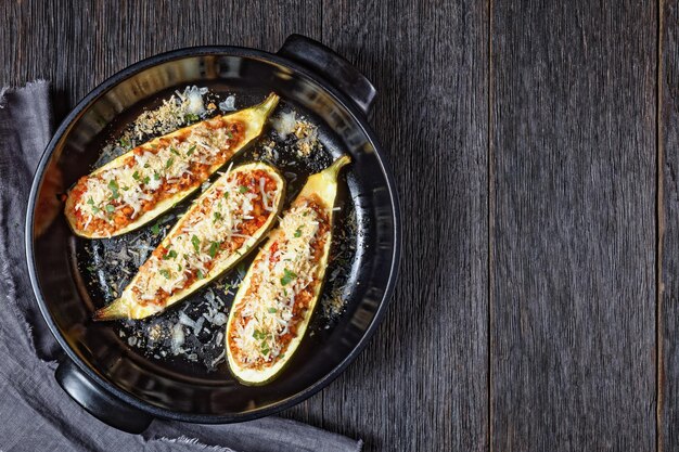 Zucchini boats stuffed with ground meat, chopped tomatoes, and cheese in a black baking dish on a wooden table,  italian cuisine