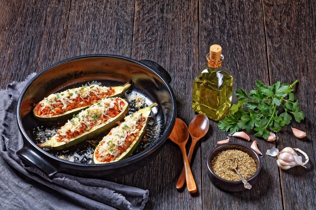 Zucchini boats stuffed with ground meat, chopped tomatoes, and cheese in a black baking dish on a wooden table,  italian cuisine