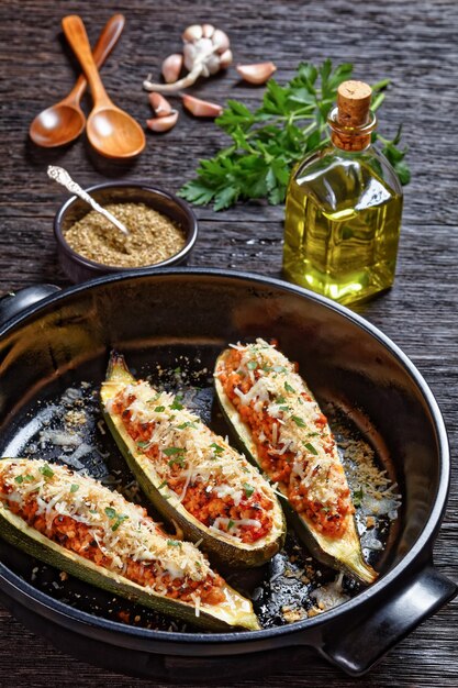 Zucchini boats stuffed with ground meat, chopped tomatoes, and cheese in a black baking dish on a wooden table,  italian cuisine