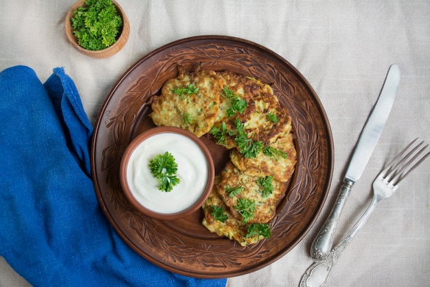 Zucchini fritters. Vegetarian zucchini crepes served with fresh herbs and sour cream. Light background.