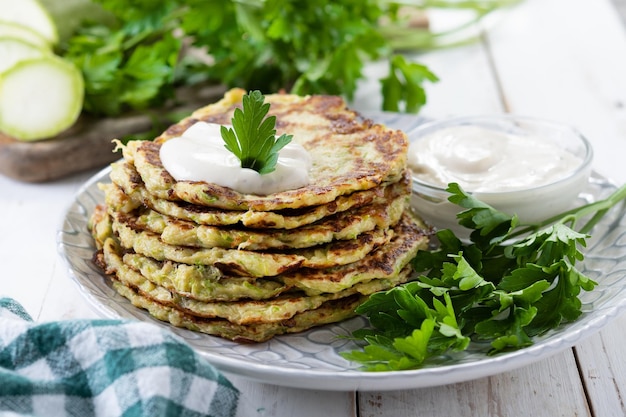 Frittelle di zucchine con salsa allo yogurt sul tavolo di legno bianco