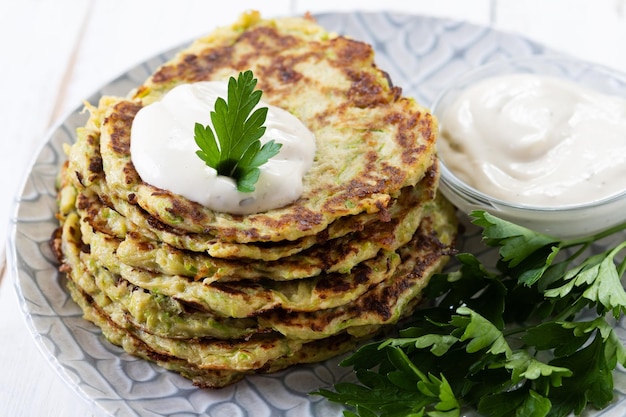 Zucchini fritters with yogurt sauce on white wooden table