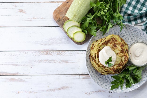 Zucchini fritters with yogurt sauce on white wooden table