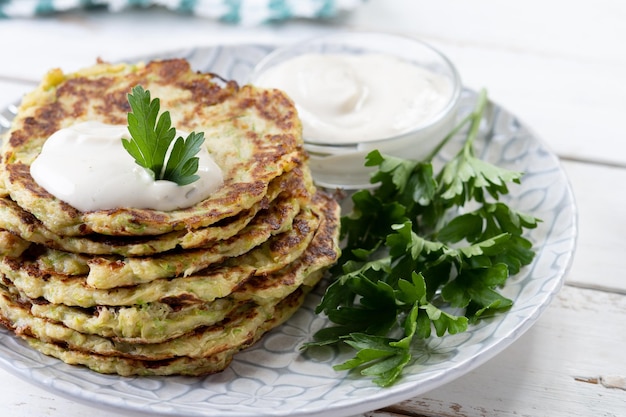 Frittelle di zucchine con salsa allo yogurt sul tavolo di legno bianco