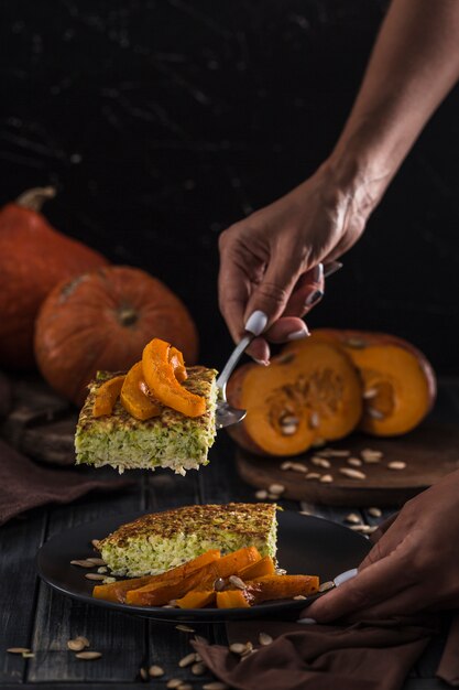 Zucchini pie with baked pumpkin on a spatula in women's hands in the kitchen, on a dark wooden copyspace close-up with copyspace.