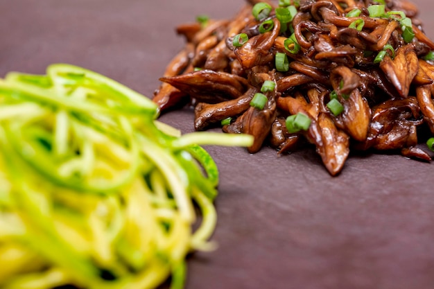 Spaghetti di zucchine con shimeji su lastra di pietra nera.