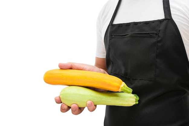 白い背景の調理コンセプトに分離されたエプロンの男の手でズッキーニ野菜