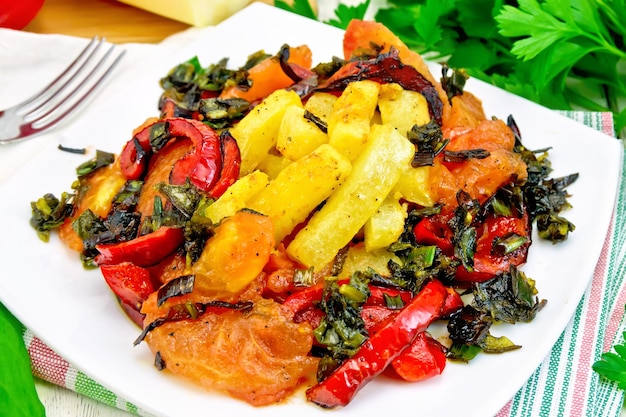 Zucchini with tomatoes, pepper and sorrel fried Greek in a plate on a napkin, fork, parsley on a wooden boards background