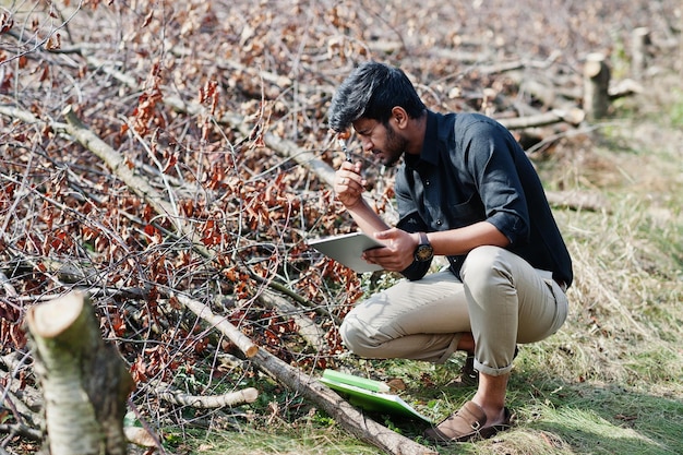 Zuid-Aziatische agronomist-boer met klembord die omgehakte bomen in de boerderijtuin inspecteert Landbouwproductieconcept