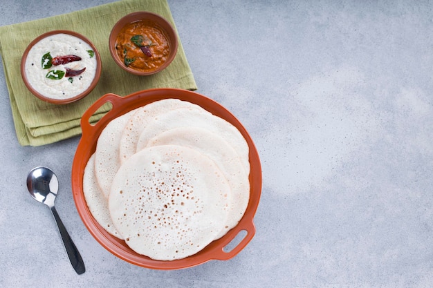 Zuid-Indiase traditionele ontbijt Dosa of Thattu dosa gemaakt met behulp van gietijzeren dosa thawa gerangschikt in een servies met bijgerecht witte kokos chutney en ui chutney op witte gestructureerde achtergrond