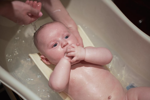 Zuigelingsjongetje gewassen in klein bad, moederhanden in de buurt, van bovenaf bekijken