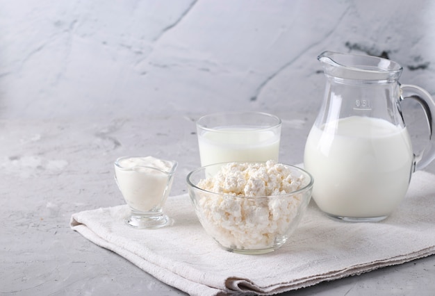 Zuivelproducten: melk, kefir of ayran, kwark en zure room in een transparante kom, kruik en glas op een grijze ondergrond, ruimte voor tekst, close-up