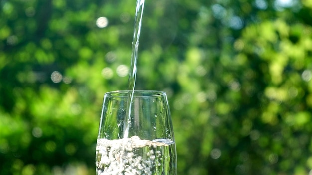 Zuiver water gegoten in glas close-up in zonlicht groene natuur achtergrond. Helder vers drinkwater