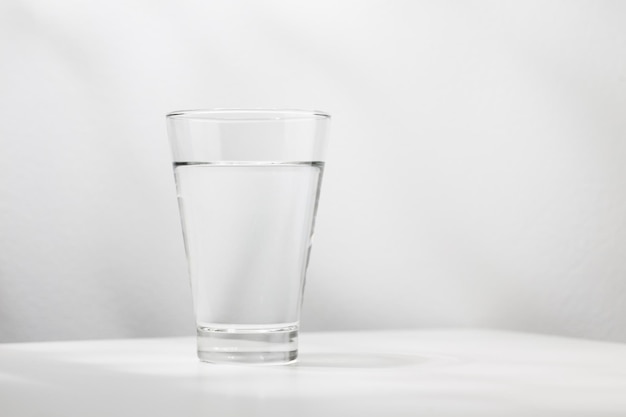 Zuiver water in het glas ligt op de witte houten tafel.