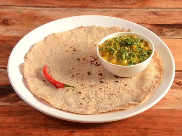 Zunka Bhakar Pithla or pitla popular vegetarian recipe from India served in rustic wooden background selective focus