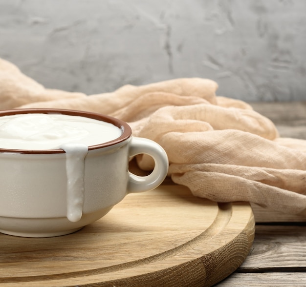 Zure room in een bruine ceramische kom met een houten lepel op een houten plank, nuttig product van gefermenteerde melk