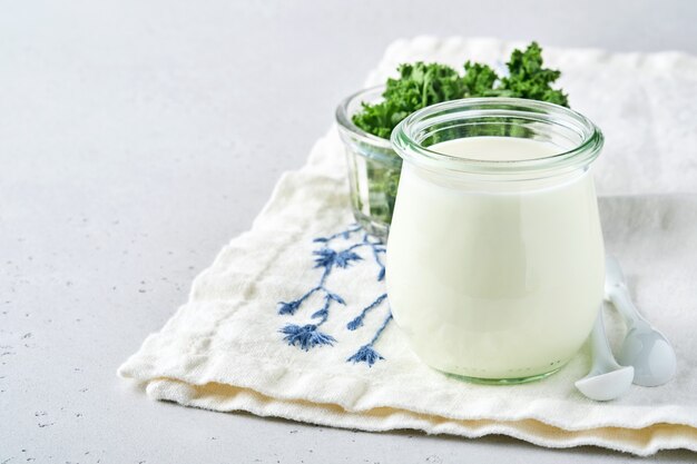 Zure room of natuurlijke yoghurt in een glazen pot met lepels, gezondheids- en dieetconcept op lichtgrijze leisteenachtergrond.