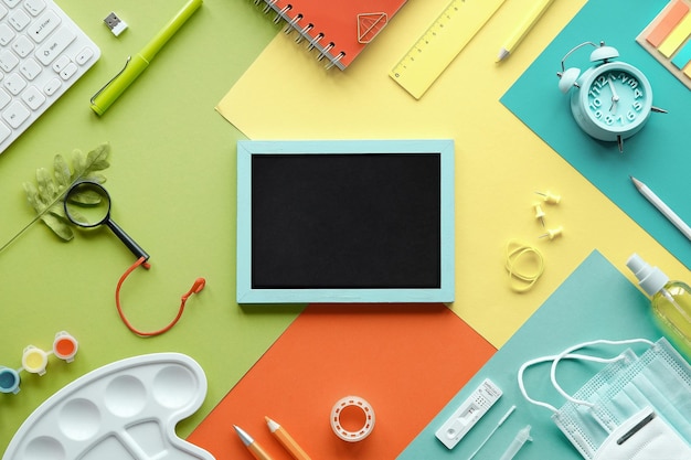 Zuruch in die Schule means or back to school in German language Concept top view with chalk text on blackboard Corona quick tests mask stationary Flat lay on layered colored paper background