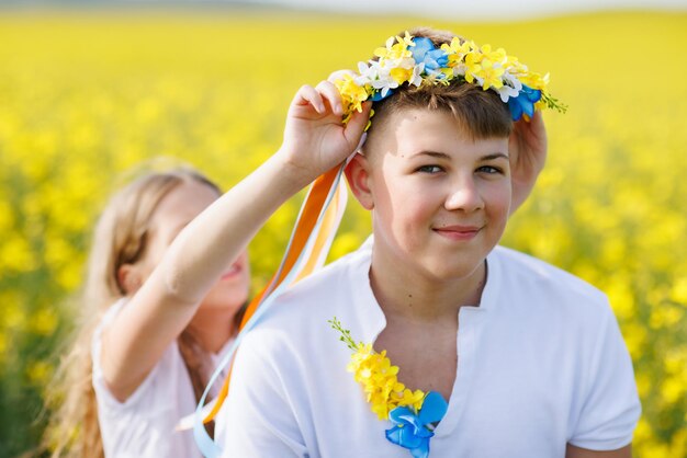 Zus vlecht linten in Oekraïense krans op het hoofd van haar tienerbroer tegen de achtergrond van velden en lucht