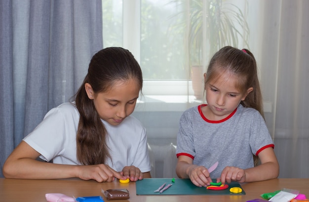 Zusjesmeisjes boetseren thuis aan tafel uit klei