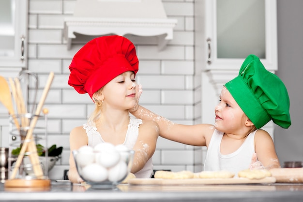 Zusters die in heldere kokhoeden samen in een keuken bakken