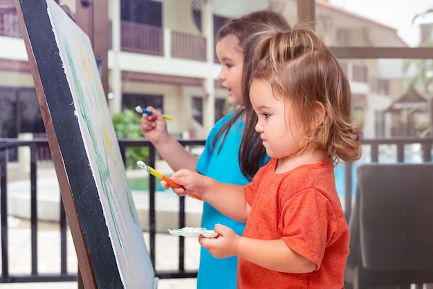 Zusters kinderen tekenen samen met verf op een ezel