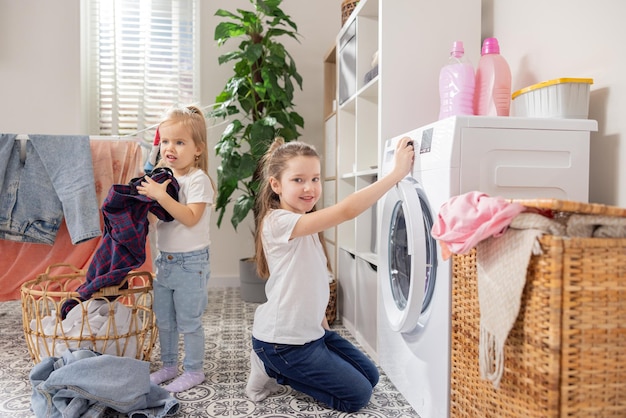 Zusters schoon in was meisje knielt bij wasmachine vol met kleurrijke kleding