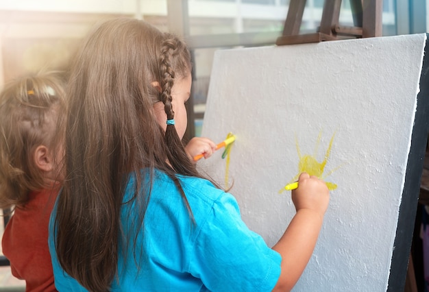 Zusterskinderen schilderen samen op canvas op een ezel