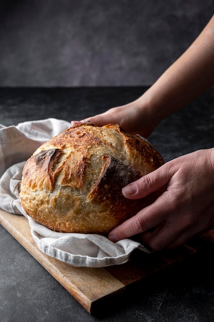 Zuurdesem ambachtelijk zelfgebakken brood, vrouwelijke handen met brood op donkere achtergrond.