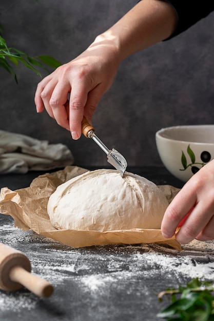 Zuurdesembrood thuis koken. Vrouwelijke hand die vers gerezen brooddeeg snijdt met een kreupelheid, klaar om te bakken.