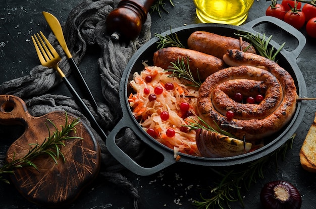 Zuurkool en gegrilde worstjes met rozemarijn en veenbessen op een zwarte plaat. Traditioneel Duits gerecht. Bovenaanzicht. Op een zwarte stenen achtergrond.