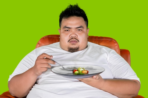 Zwaarlijvige man ziet er ongelukkig uit om salade in de studio te eten