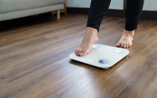 Zwaarlijvige vrouw met vet overstuur verveeld van een dieet Gewichtsverlies mislukt Vet dieet en weegschaal trieste Aziatische vrouw op weegschaal thuis gewichtscontrole