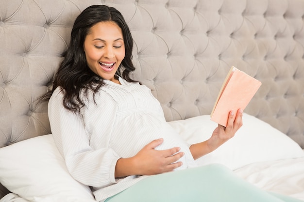 Zwanger brunette die een boek op het bed lezen