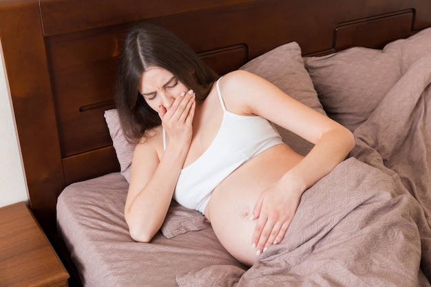 Zwanger lijden met misselijkheid Zwangerschapssymptomen verwachting toxicose Jonge brakende vrouw zittend op bed ouderschap concept