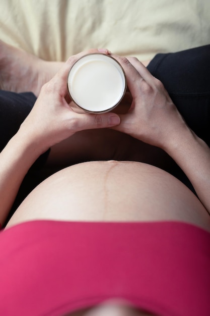 Zwanger meisje dat in bed zit en een glas melk in de hand houdt zwangerschapsochtend