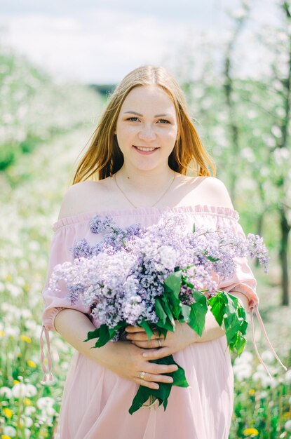 Zwanger meisje in een roze jurk in een bloementuin met een sering