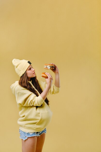 Zwanger meisje in gele kleren met hamburgers in haar handen op een gele achtergrond